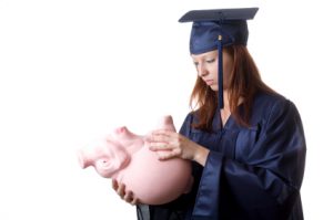 A graduate trying to remove saved money from her piggy bank. Isolated on white.